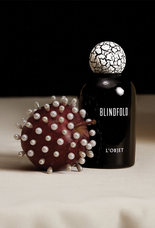 Black bottle labeled 'Blindfold' by 'L'Objet' with a textured cap on a beige surface.