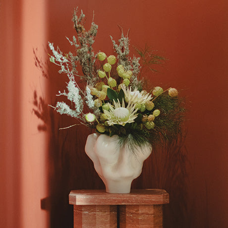 Floral arrangement in a white vase on a wooden stand against a red wall