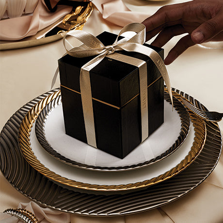 Black gift box with a gold ribbon on a decorative plate