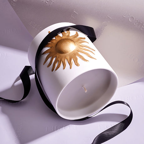 White candle with gold sun design and black ribbon on a light gray background