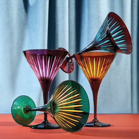 Colorful glass goblets on a red surface with a light blue curtain background